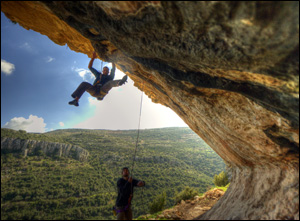 Photo of two men climbing a rock overhang.